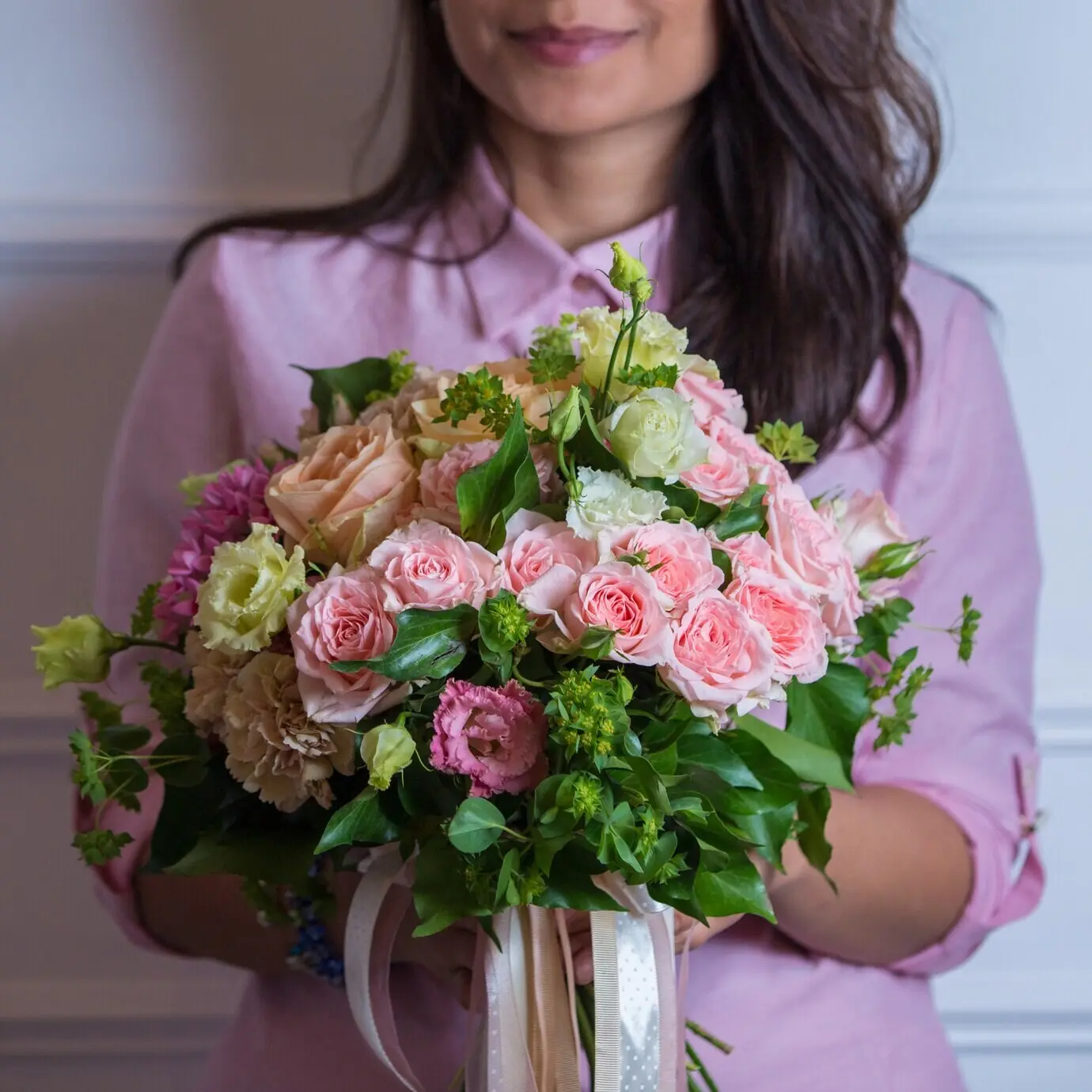 A bouquet of pink-toned roses in a woman's hands.