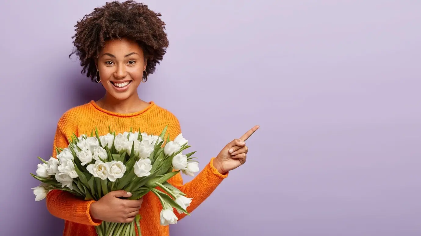 An indoor shot of a happy young female model with an Afro hairstyle, pointing away with her index finger.