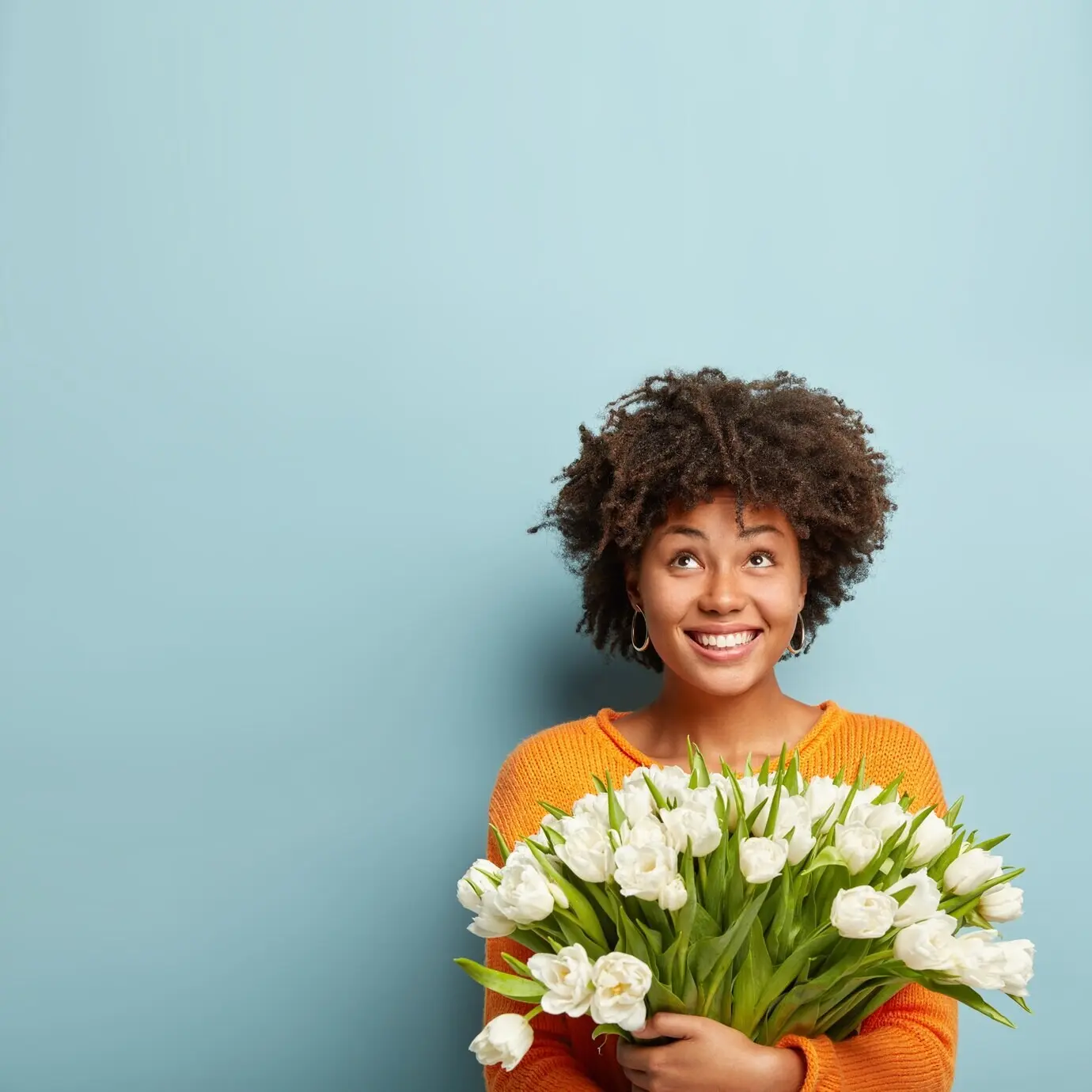 A young woman with an Afro hairstyle holding a bouquet of white flowers.